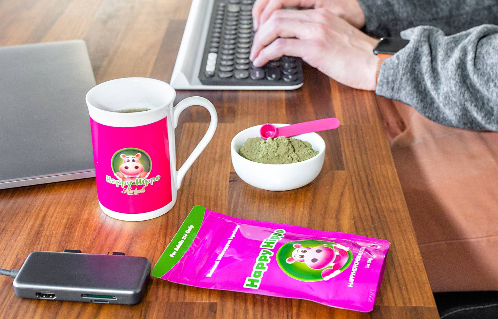 Featured image depicting a packet of Happy Hippo brand kratom powder, and a cup of kratom tea next to someone's keyboard and computer desktop at work.