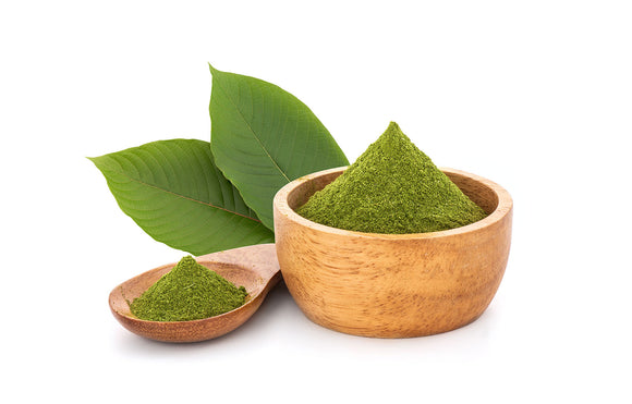 Featured Image depicting a bamboo wooden bowl containing a heap of Green Maeng Da Kratom Powder; sitting next to the bowl is a wooden spoon, as well as a couple of raw kratom leaves.