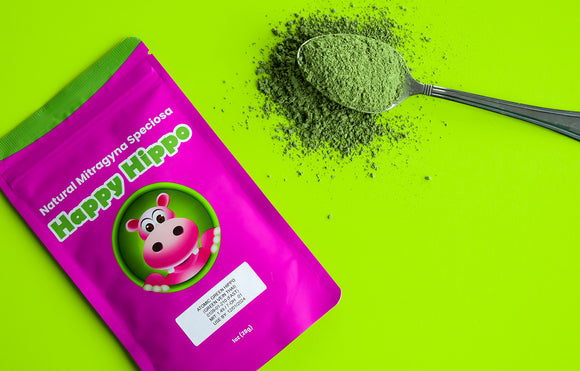 Featured image depicting a 4oz packet of Happy Hippo brand, Green Thai Kratom Powder, next to which sits a heaping spoon filled with loose green thai kratom powder, against a neon green background.