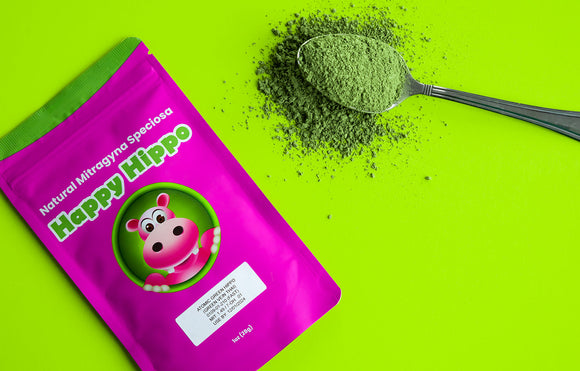 Featured image depicting a 4oz packet of Happy Hippo brand, Green Thai Kratom Powder, next to which sits a heaping spoon filled with loose green thai kratom powder, against a neon green background.