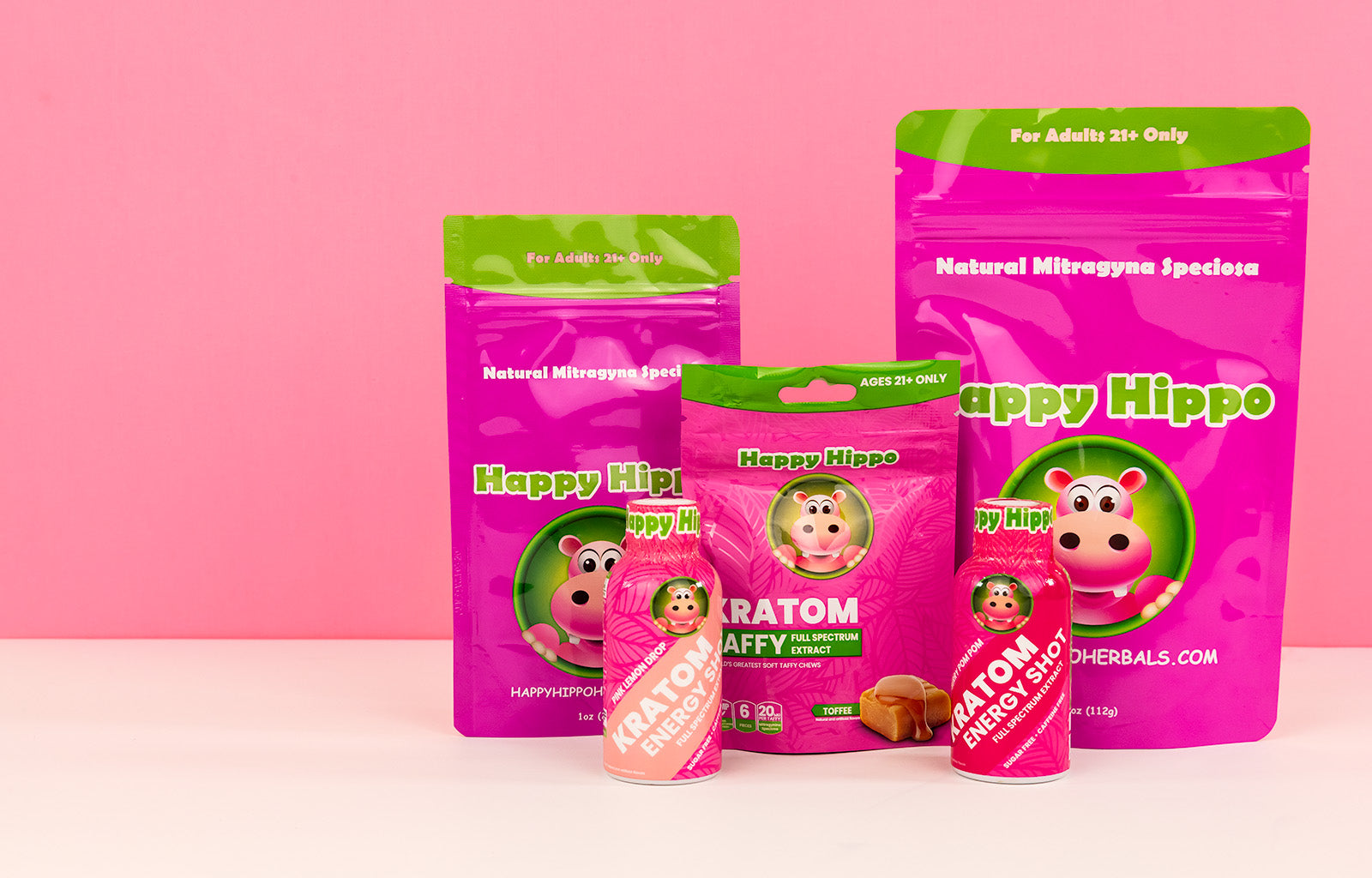 Featured image depicting several Happy Hippo branded products, including 1oz and 4oz packets of green maeng da kratom powder, a packet of 20mg toffee flavored taffy chews, and two kratom extract - kratom energy shots (KShot) on a white countertop.
