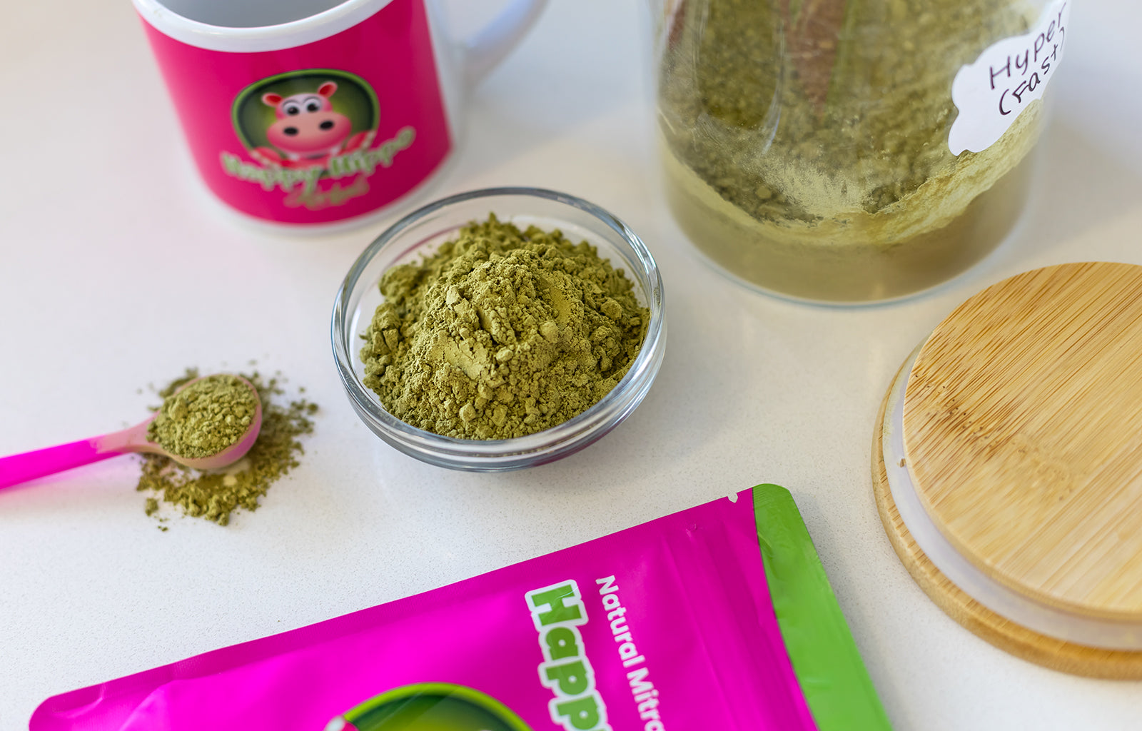 Featured image depicting an assortment of Happy Hippo brand Green Maeng Da Kratom Powder, next to which sit a small ramekin containing a heap of Green Vein Maeng Da, and a Happy Hippo branded coffee cup.