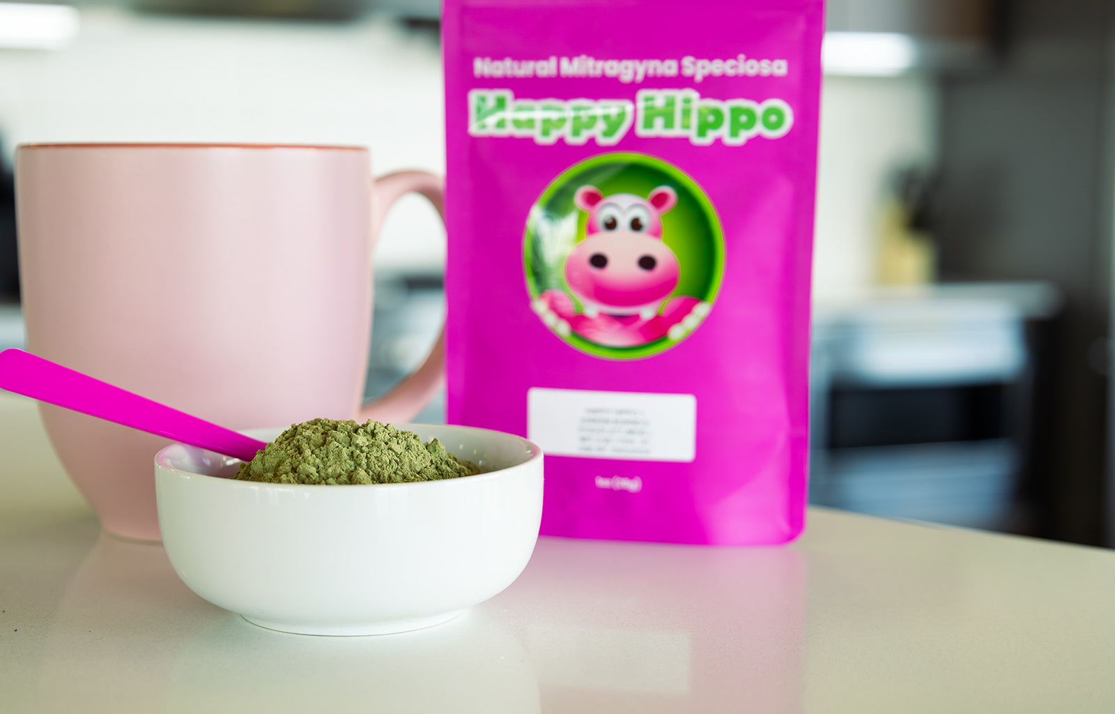 Featured image depicting a Happy Hippo branded packet of Malay Kratom sitting on a kitchen counter. A pink kratom tea cup, and a bowl of loose Malay Kratom Powder sits in the foreground.