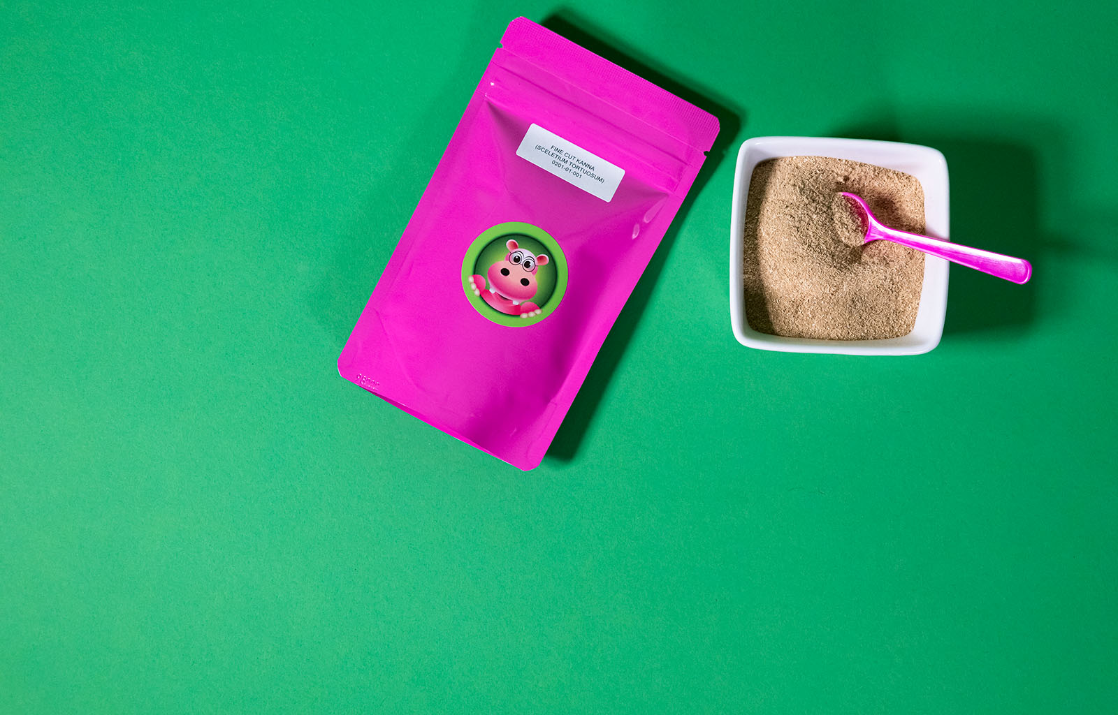 Featured image depicting a 4oz Packet of Happy Hippo brand Fine Cut Kanna Powder, and a ceramic bowl filled with loose kanna powder sitting against a green background; a 1 gram measuring scoop rests inside the bowl of loose kanna powder.