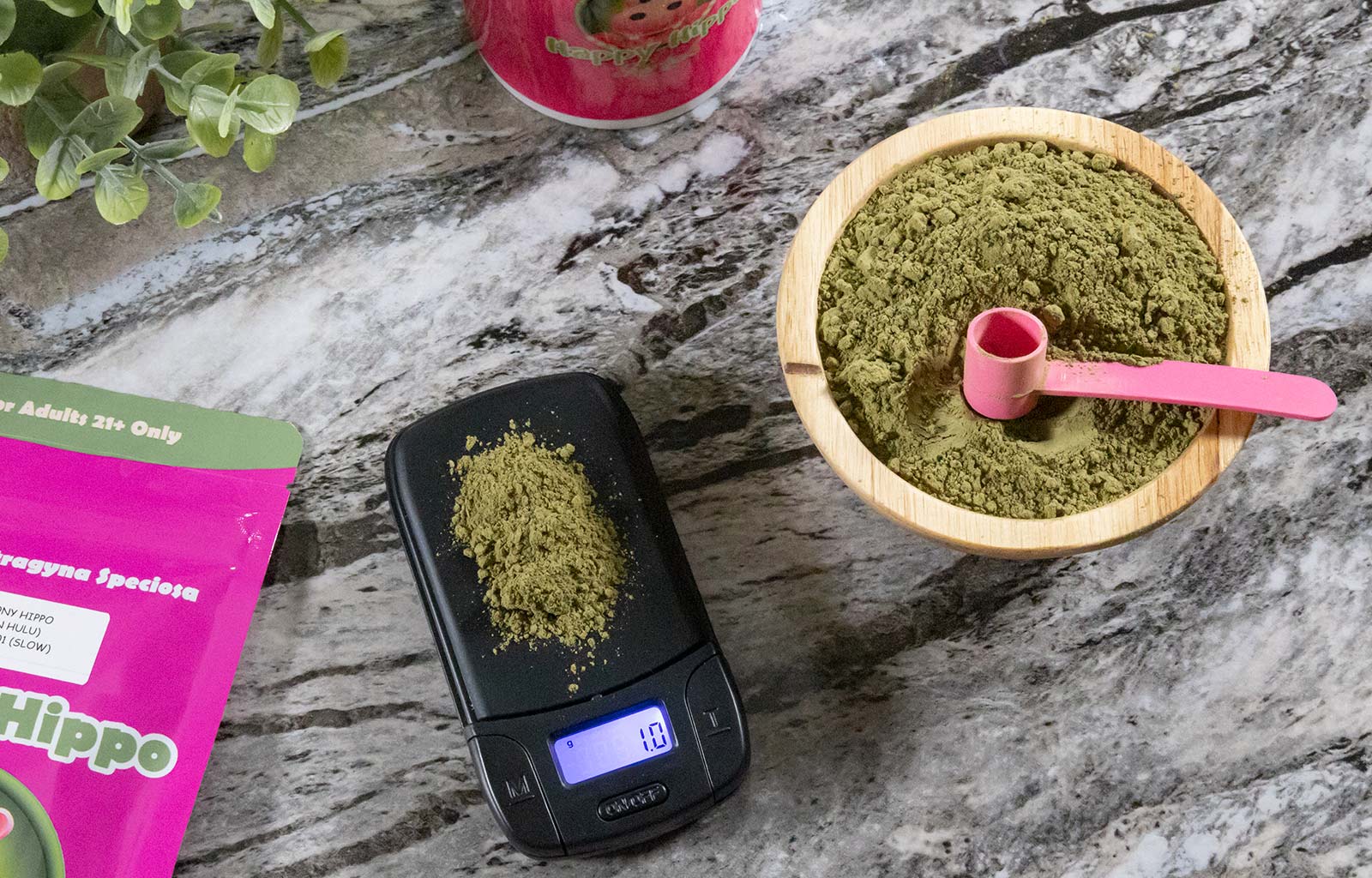 Featured Image depicting a bowl of green maeng da kratom, along side a measuring scoop, digital weight scale, and packet of happy hippo kratom powder