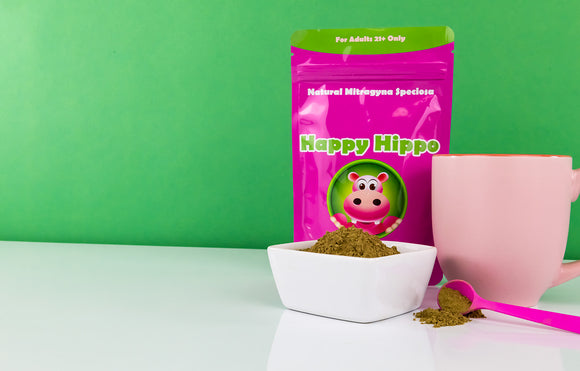 Featured image depicting a clean white counter top, with a white bowl of Thai Kratom Powder. Next to the bowl is a pink teacup, a 1 gram measuring scoop, and a 4oz branded packet of Happy Hippo Green Thai Kratom Powder