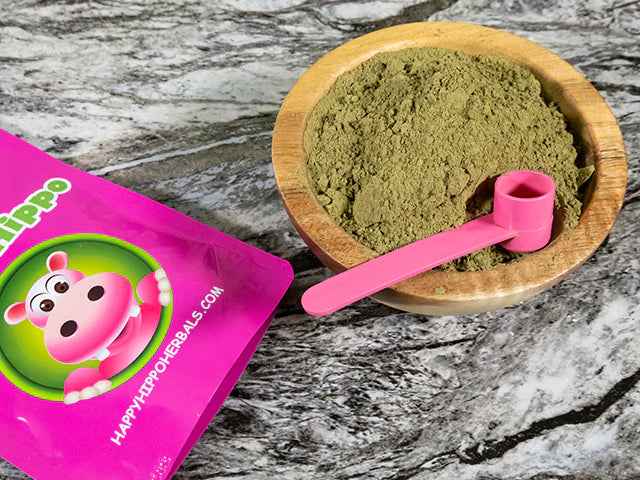 Product image depicting a wooden bowl of loose happy hippo kratom powder with a 1 Gram pink measuring scoop resting inside
