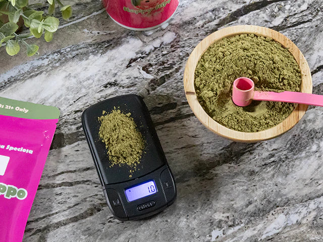Product image depicting a digital weight scale sitting on a counter top, measuring 1 gram of loose Happy Hippo Herbals brand kratom powder